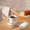 A coffee cup, a croissant, and a spoon are arranged on a wooden table, with a chair and a book in the background. Náhled obrázku produktu