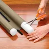 Hands are cutting a draft stopper with scissors on a wooden floor. Anteprima dell’immagine prodotto