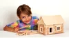 A young girl is sitting at a table with a wooden log cabin building set. Anteprima dell’immagine prodotto