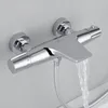 A chrome shower thermostat faucet mounted on a light gray wall, with water flowing from the spout. Produktbild-Vorschau