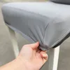 A hand is shown stretching a grey chair cover over the seat of a chair. Náhled obrázku produktu