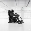 A person wearing a racing suit and helmet sits in a racing simulator cockpit, holding the steering wheel. Produktbild-Vorschau