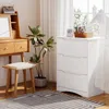 A white dresser with three drawers is placed next to a wooden vanity with a mirror and stool. A plant is in a pot between the two pieces of furniture. A striped rug is on the floor. Podgląd zdjęcia produktu