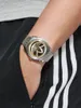 A person's wrist wearing a watch, with part of their black and white striped pants visible. Podgląd zdjęcia produktu