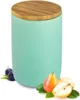 A turquoise ceramic storage jar with a wooden lid, placed on a white background with some fruits and leaves. Náhľad obrázku produktu