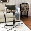 A folding table with a marble-like top is set up next to a sofa, holding a teapot, cup, and plate of waffles. Another set of folding tables is stacked behind it. Produktbild-Vorschau