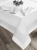 A white tablecloth with a subtle striped pattern is laid out on a wooden table, with a teacup, saucer, and glasses placed on it. Produktbild-Vorschau