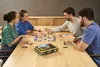 Four people playing a board game at a wooden table. Produktbild-Vorschau