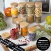 A collection of spice jars with wooden lids, along with some loose spices and a marker, arranged on a surface. Produktbild-Vorschau