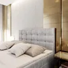 A close-up view of a bed with a tufted headboard, pillows, and a bedside table with a lamp. Produktbild-Vorschau