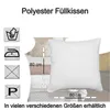A white pillow is shown in the center, with care instructions and size indicators on the left and bottom. The background shows a bedroom setting with other pillows and bedding. Produktbild-Vorschau