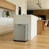 A modern kitchen with a stainless steel automatic trash can in the foreground, next to a marble island. Kitchen cabinets and a sink are visible in the background. Produktbild-Vorschau