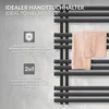 A close-up of a black towel warmer with two peach-colored towels draped over it, set against a textured gray wall. Text overlays highlight product features. Produktbild-Vorschau