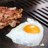 A close-up shot of bacon and a fried egg cooking on a grill. Podgląd zdjęcia produktu