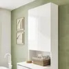 A white cabinet with two doors and an open shelf below, placed against a green wall. There are two framed pictures on the wall and a basket with items on the shelf. Produktbild-Vorschau
