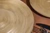 A close-up view of two gold-colored dessert plates with a textured, concentric ring design, placed on a brown surface. A black knife and fork are visible in the lower right corner. Podgląd zdjęcia produktu