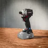 A cordless impact driver with a battery pack attached, resting on a wooden surface against a concrete wall. Produktbild-Vorschau