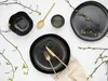 A flat lay of black stoneware dinnerware with gold cutlery and decorative branches with buds. Náhľad obrázku produktu