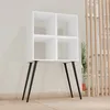 A white cube shelf unit with four compartments, supported by four black, angled metal legs, is shown in a room with a light-colored wall and wooden floor. Voir les images du produit