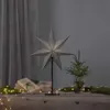A star-shaped lamp and a small Christmas tree are displayed on a wooden surface, with gifts and fairy lights. Podgląd zdjęcia produktu