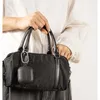 A person is holding a black handbag with an accessory attached. Voir les images du produit