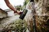 A person is filling a GRAYL water purifier with water from a natural spring. Podgląd zdjęcia produktu