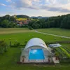 A covered swimming pool in a rural setting with a village and castle in the background. Produktbild-Vorschau