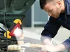 A mechanic is working on a car engine, illuminated by a warning triangle light. Voir les images du produit