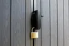 A close-up of a black gate latch with a gold padlock attached. Náhled obrázku produktu