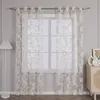 A sheer, white lace curtain with a floral pattern hangs in front of a window. Produktbild-Vorschau