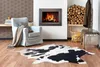 A cozy living room scene with a fireplace, armchair, and a cowhide rug. Produktbild-Vorschau
