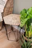 A hexagonal side table with a geometric metal base, placed next to a wicker chair and a large potted plant. Náhled obrázku produktu