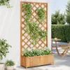 A wooden planter box with a trellis attached, filled with plants, stands against a white wall on a patio. A small round table and chair are visible in the background. Náhľad obrázku produktu