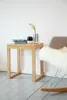 A small wooden stool with books and a vase on top, next to a rocking chair with a sheepskin throw. Produktbild-Vorschau