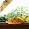 A wooden bowl filled with birdseed sits on a wooden surface, with a blurred background of greenery and yellow flowers. Produktbild-Vorschau