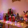 Christmas decorations including gift boxes, trees, and a reindeer, illuminated by colorful string lights. Produktbild-Vorschau
