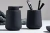 A black soap dispenser and a black cup holding makeup brushes are displayed on a white surface with a gray towel in the background. Produktbild-Vorschau