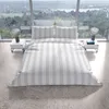 A bed with striped bedding is set up in a modern room with large windows overlooking a landscape. Produktbild-Vorschau