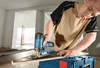 A man is using a jigsaw to cut a piece of wood in a room under renovation. Produktbild-Vorschau