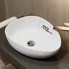 A white oval sink with a gold drain is placed on a dark gray countertop. Anteprima dell’immagine prodotto