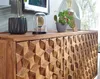 A close-up view of a wooden sideboard with a geometric carved pattern on its doors and drawers. Decorative items, including a potted plant and a glass dome with an object inside, are placed on top. Anteprima dell’immagine prodotto