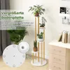 A multi-tiered plant stand with plants on a white and gold frame, placed in a room with a desk and books in the background. Náhled obrázku produktu