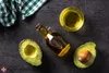 Avocado oil and avocados are laid out on a dark surface. Anteprima dell’immagine prodotto