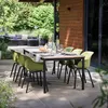 An outdoor dining set with green chairs and a wooden-topped table on a patio, surrounded by greenery and a modern house. Anteprima dell’immagine prodotto