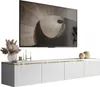 A modern white TV cabinet with gold trim, mounted on a wall, with a large flat-screen TV above it displaying abstract art. Decorative items like a vase with dried flowers, candles, and spheres are placed on the cabinet. Náhľad obrázku produktu