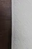 A close-up view of the edge of a white textured rug with a floral pattern, placed on a dark wooden floor. Produktbild-Vorschau