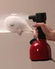 A hand holding a red and black steam cleaner spraying steam onto a white knitted whale toy. Anteprima dell’immagine prodotto