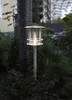 A solar-powered path light is illuminated in a garden setting at dusk, surrounded by plants and a tree trunk. Produktbild-Vorschau