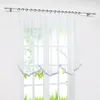 A sheer white curtain with a scalloped bottom edge trimmed in gray hangs in front of a window. Produktbild-Vorschau