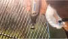 A hand is using a Dremel tool to clean a grill grate. Produktbild-Vorschau